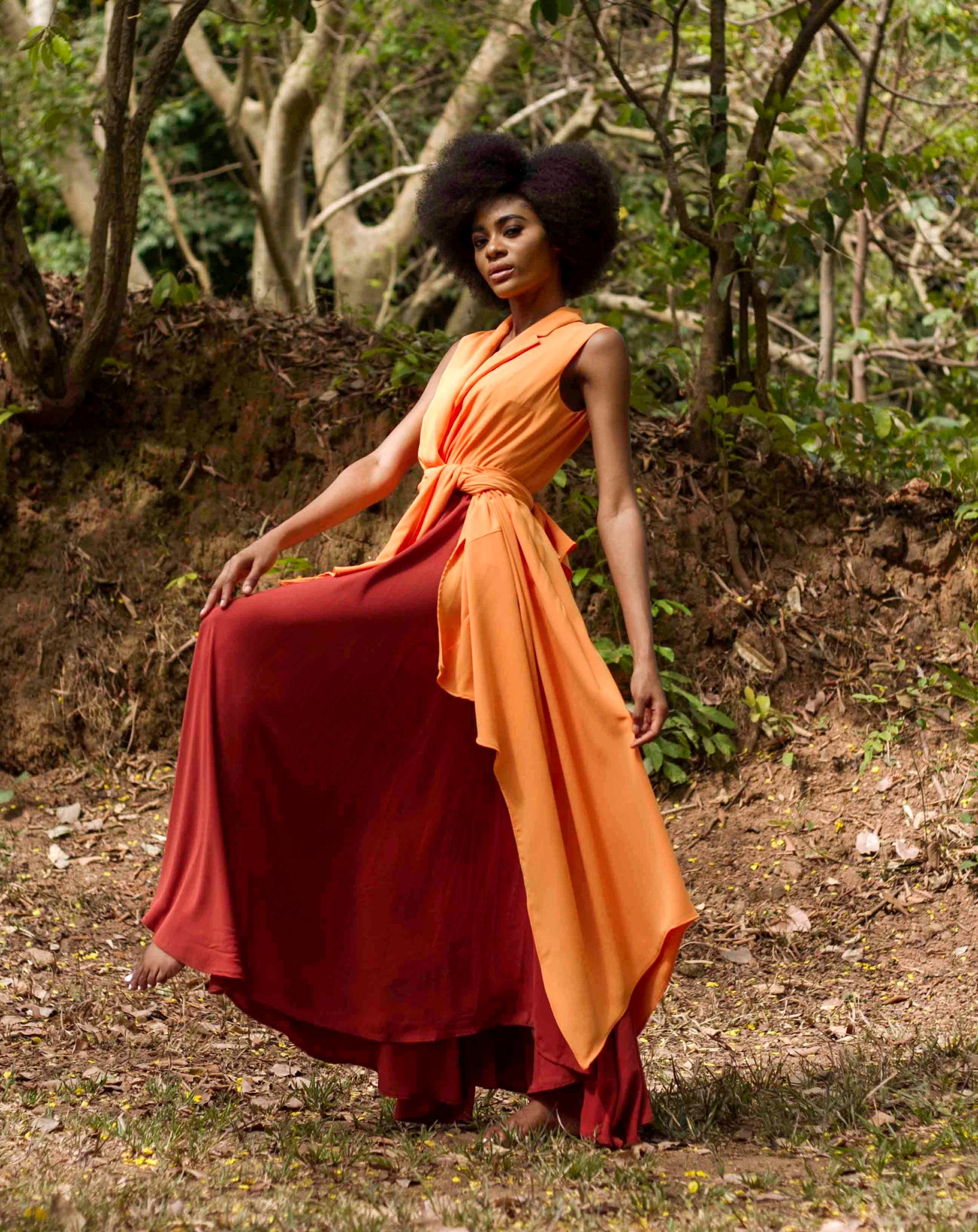 This two-layered Mata Multicoloured Dress, features an orange high-low outer layer and a maroon flared inner layer. The upper portion of the dress has a lapel collar and is accented with an invisible zipper in the back. Its casual style and sleeveless design make it a carefree and flowy gown.