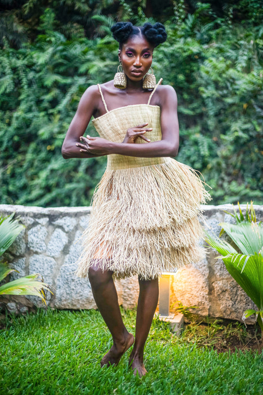 The Numa Dress is a summer and traditional dress made of raffia or straw which  embodies a unique blend of natural textures and playful elegance. The midi length adds a touch of classic sophistication, while the material choice keeps it grounded in tradition and earthiness.  This Cynthia-Abila signature Numa dress  features a relaxed fit that gently sways with movement, perfect for capturing the carefree essence of summer. Its natural color palette can range from light beige to deeper earth tones.