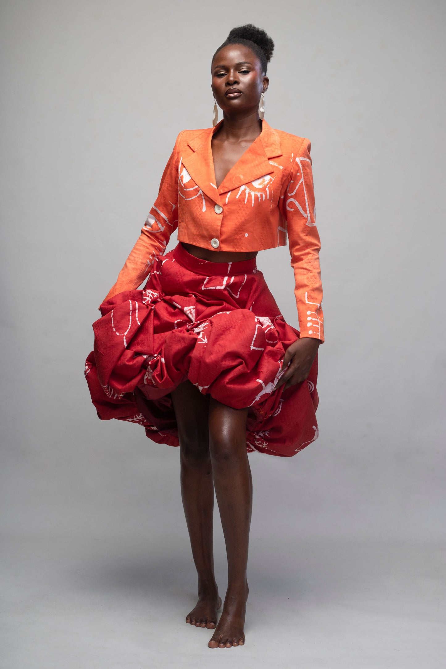 Woman wearing a bright orange blazer and red skirt against a gray background